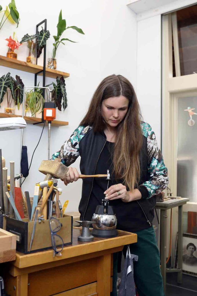 Jewelry artist Liesbeth Busman hammering gold and setting diamonds on a goldsmith workbench